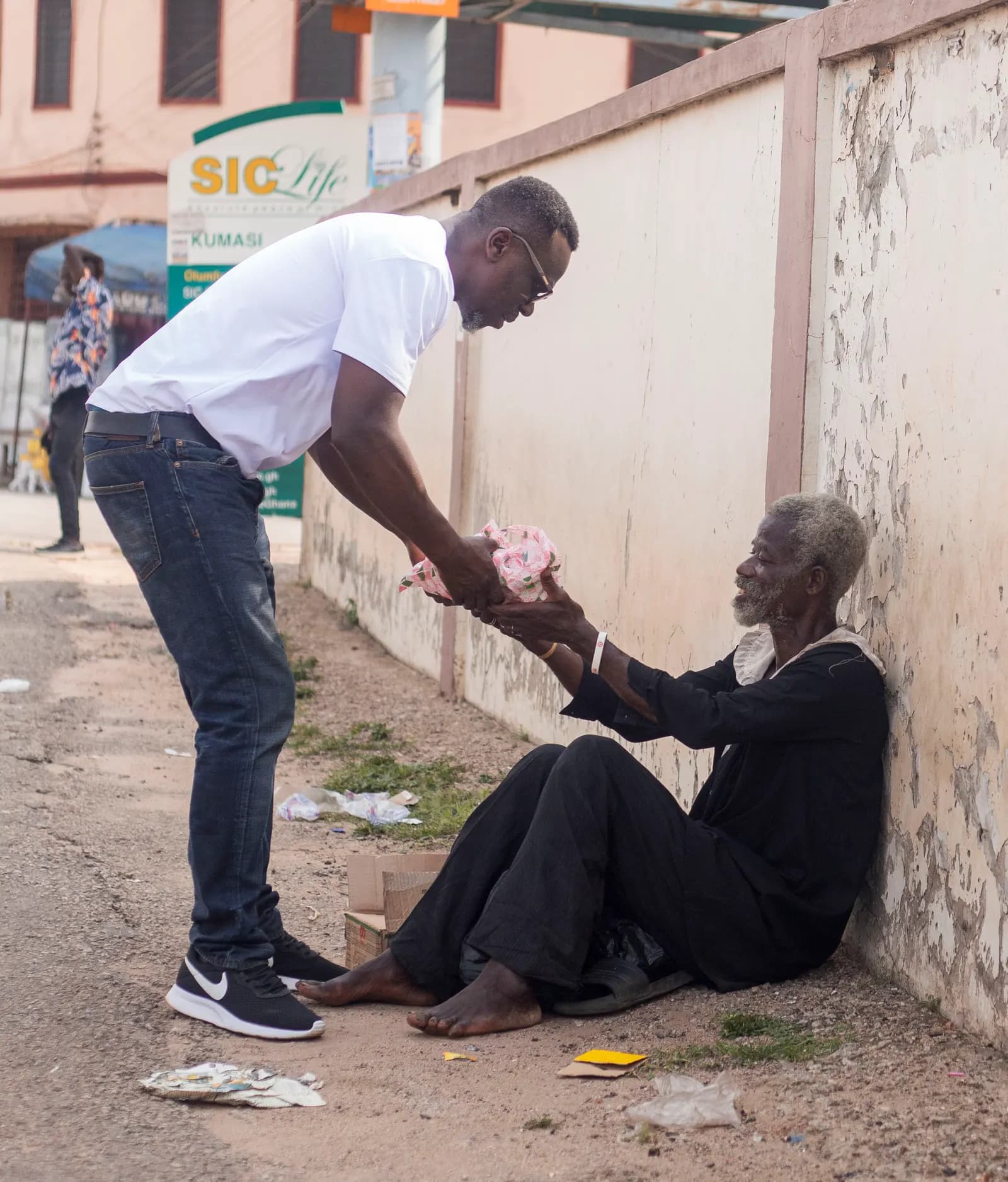Prince Asamany bending to greet an elderly woman during a community relief visit in Kumasi