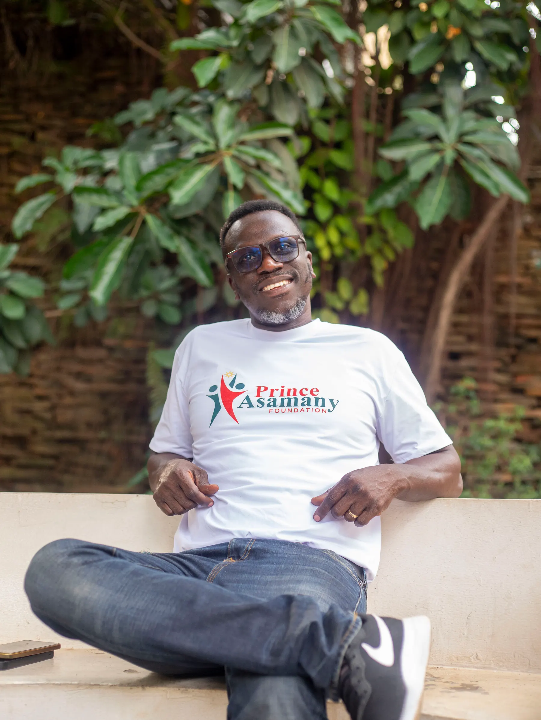 Portrait of Prince Douglas Asamany, Founder and President of the Prince Asamany Foundation, seated outdoors in a foundation T-shirt