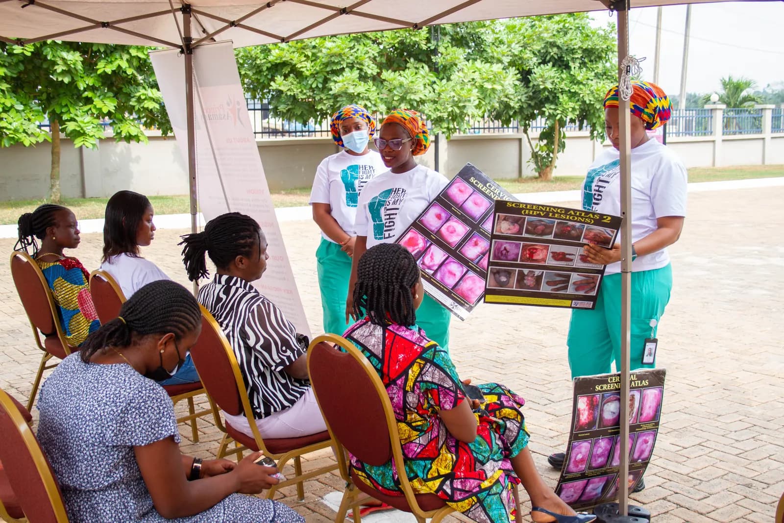Health educator presenting a cervical cancer awareness atlas to seated women at a community screening outreach